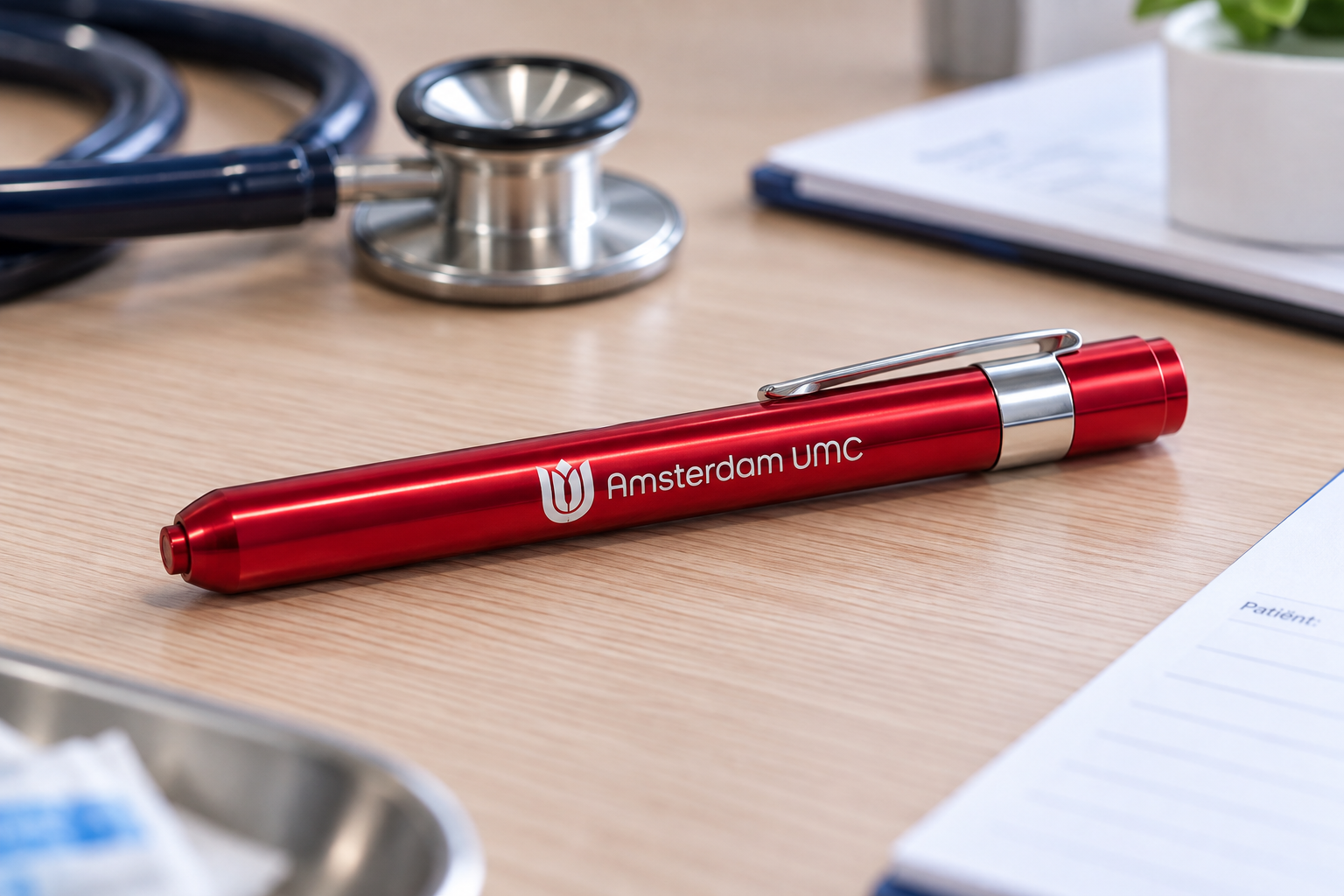 A red diagnostic penlight with a clip, used by healthcare professionals for patient examinations, resting on a wooden clinic desk.
