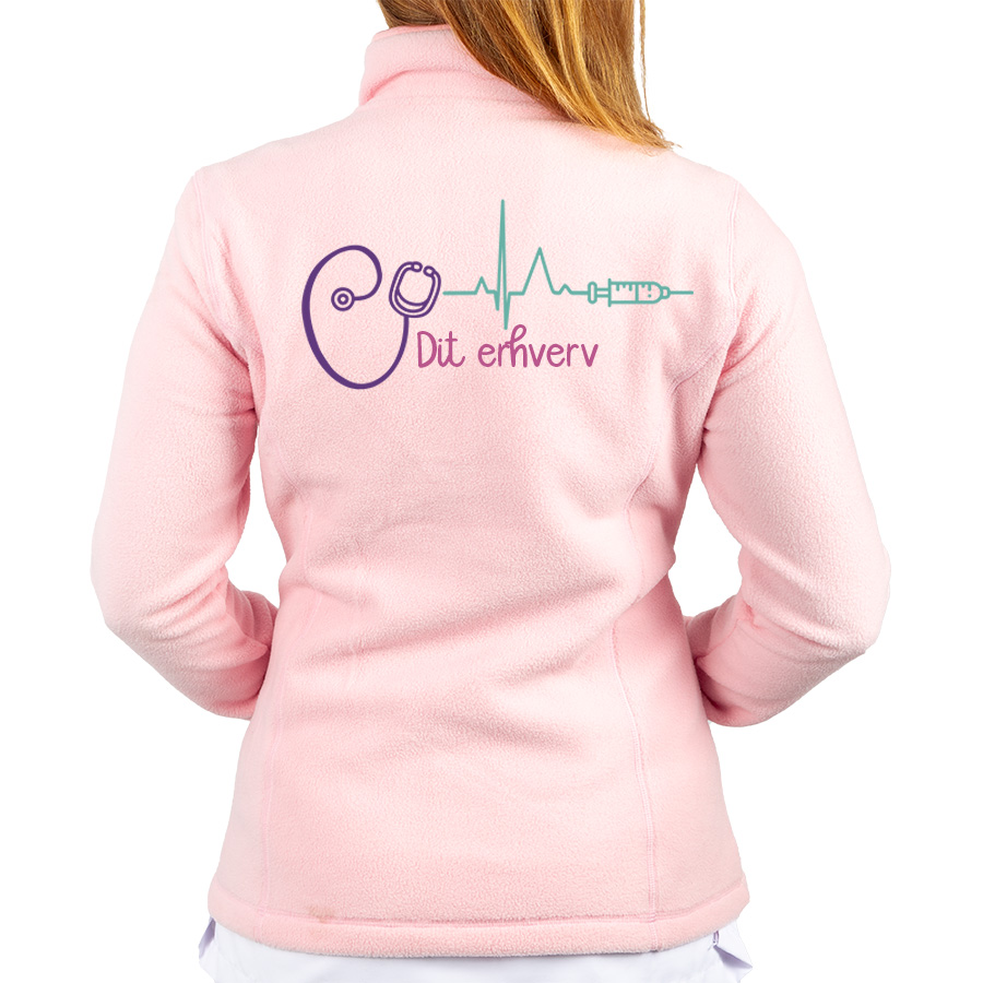 Pink fleecejakke til sygeplejersker med lilla stetoskop, grønt hjerteslag og sprøjtedesign på ryggen, ideel til komfort.